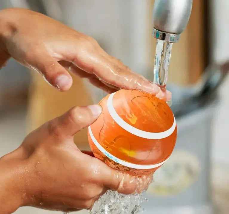 Orange interactive cat ball toy by NexiPets with white stripes, being rinsed under a faucet.